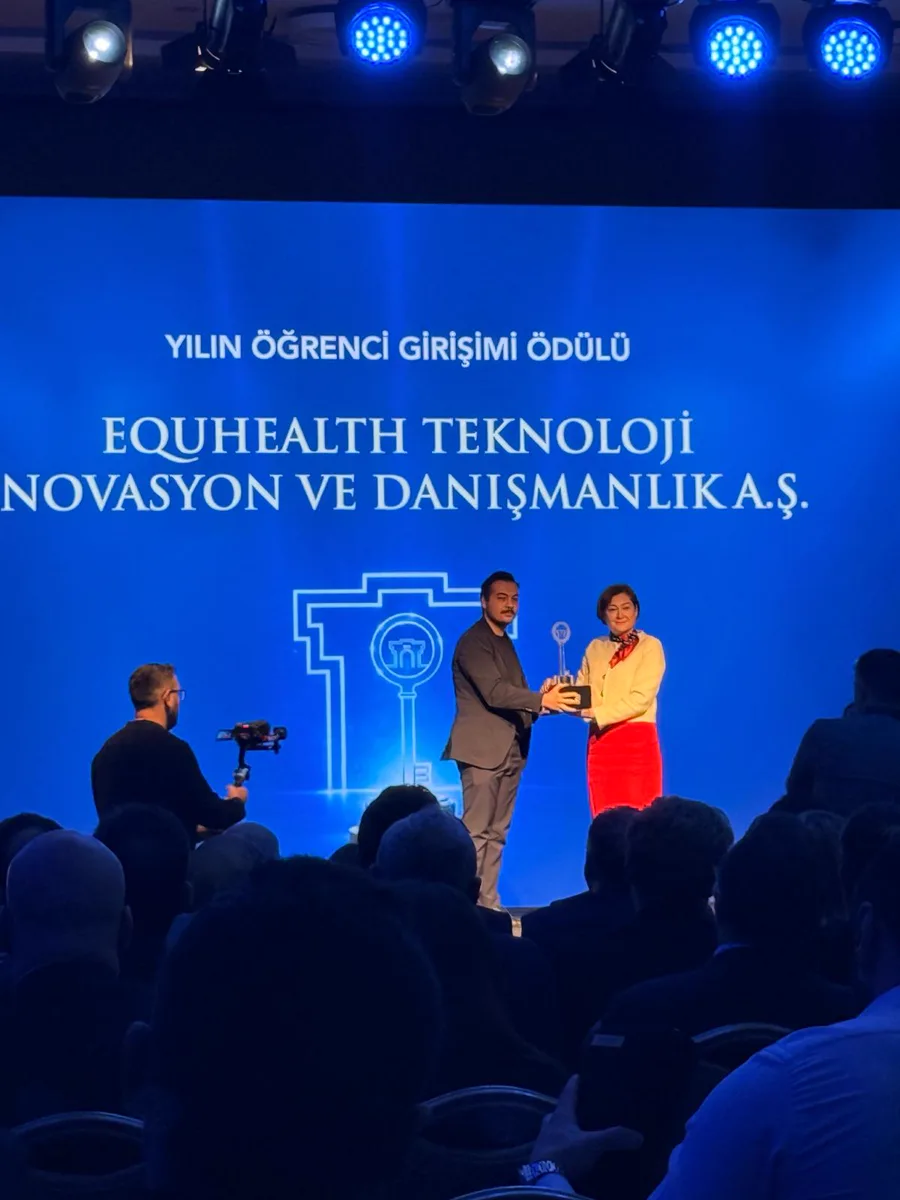 Yılın Enleri ödül töreninde sahnede, arkadaki ekranda Yılın Öğrenci Girişimi Ödülü ve EQUHEALTH yazıyor